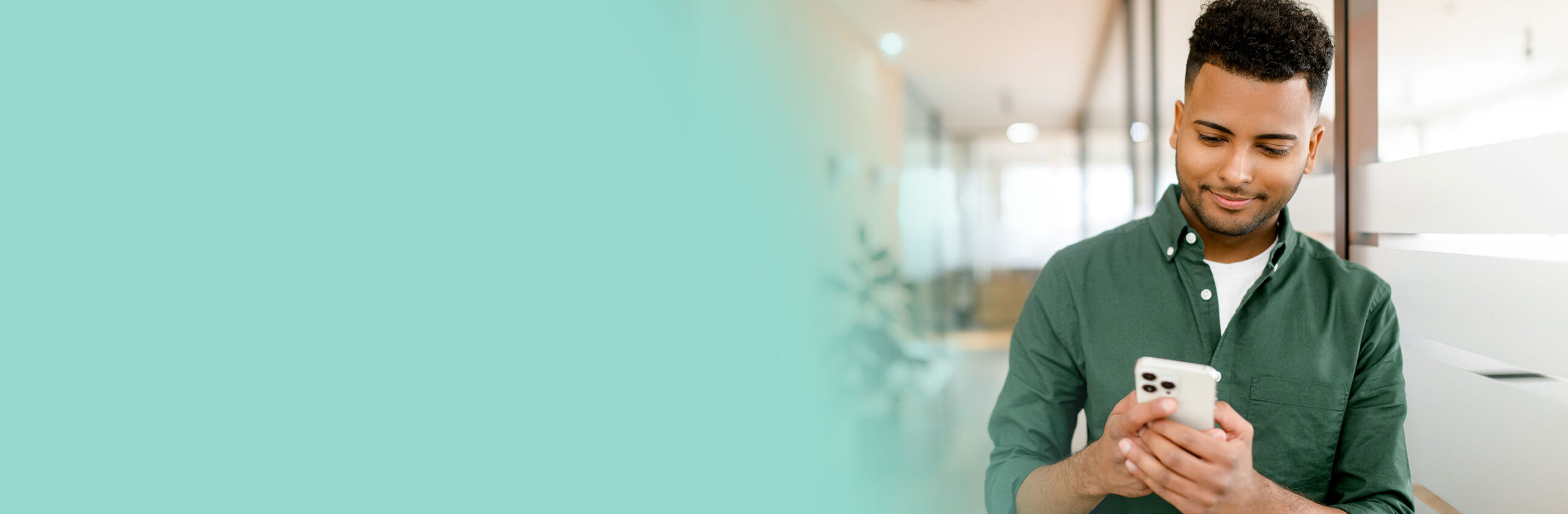 Young dark-haired man in smart casual green shirt using smartphone.